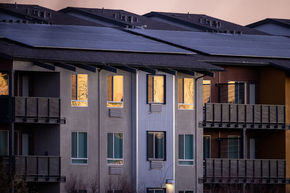 Apartment building with dark solar panels on the roof at dusk