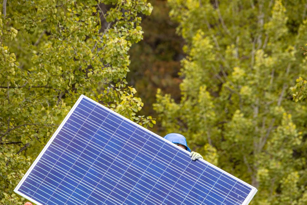 Installer carrying a solar panel across a roof