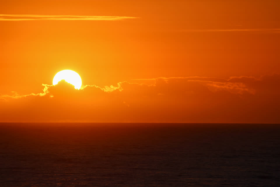 Sun setting over the horizon in deep orange sky